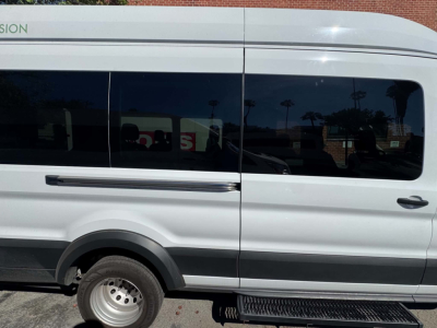 Ford Transit 350 HD passenger van side view. Visible text includes 'TRANSIT' on the front fender and a green stripe. Window tint shows reflections.
