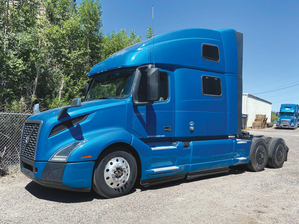 Volvo VNL 860 tractor cab in blue, sleeper configuration, side view showing front wheel, fuel tanks, and dual rear axles.