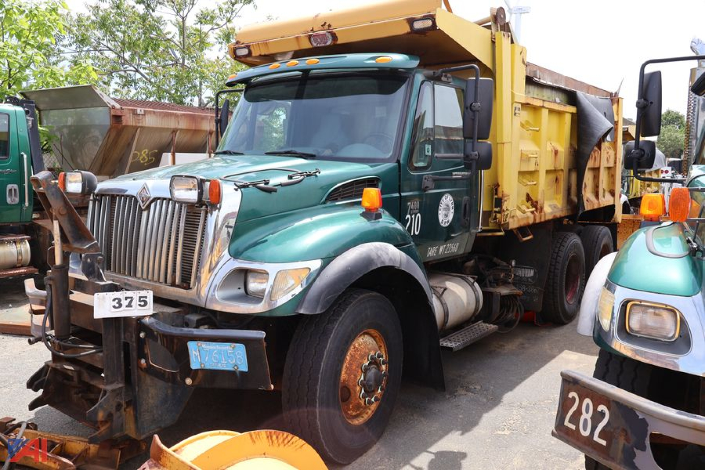 Dump truck in service bay showing green International WorkStar 7400 front with yellow dump bed and chrome grille.