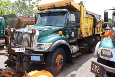Dump truck in service bay showing green International WorkStar 7400 front with yellow dump bed and chrome grille.