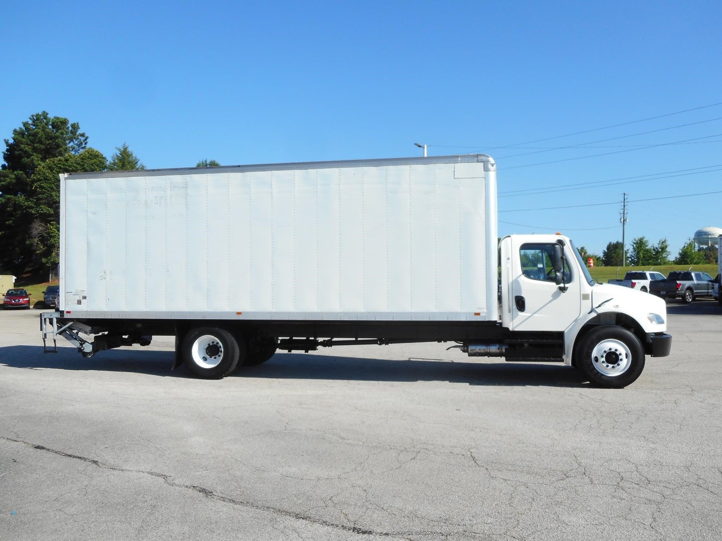 Box truck side view of a 2019 Freightliner M2 106 with a long rectangular cargo box and white cab, VIN visible in listing, box truck on paved lot.