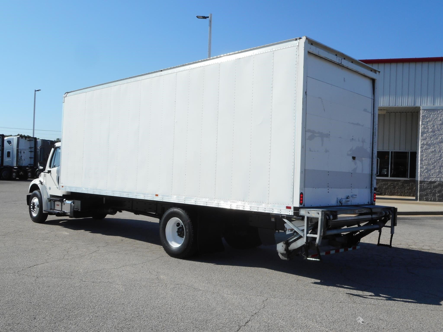 Box truck in service view showing Freightliner M2 106 box truck with white cargo box and rear underride guard