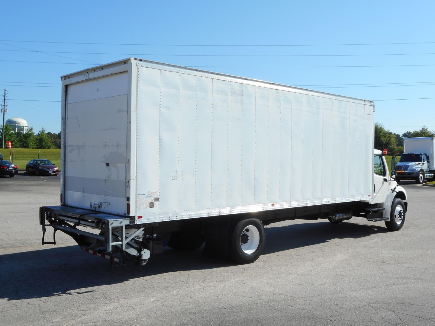Box truck rear and side view showing large cargo box on Freightliner M2 106 with white exterior and rear underrun guard.