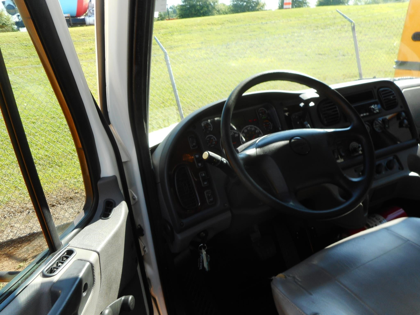 Truck cab interior of a 2019 Freightliner M2 106 showing steering wheel and dashboard from the driver's door with keys in ignition.