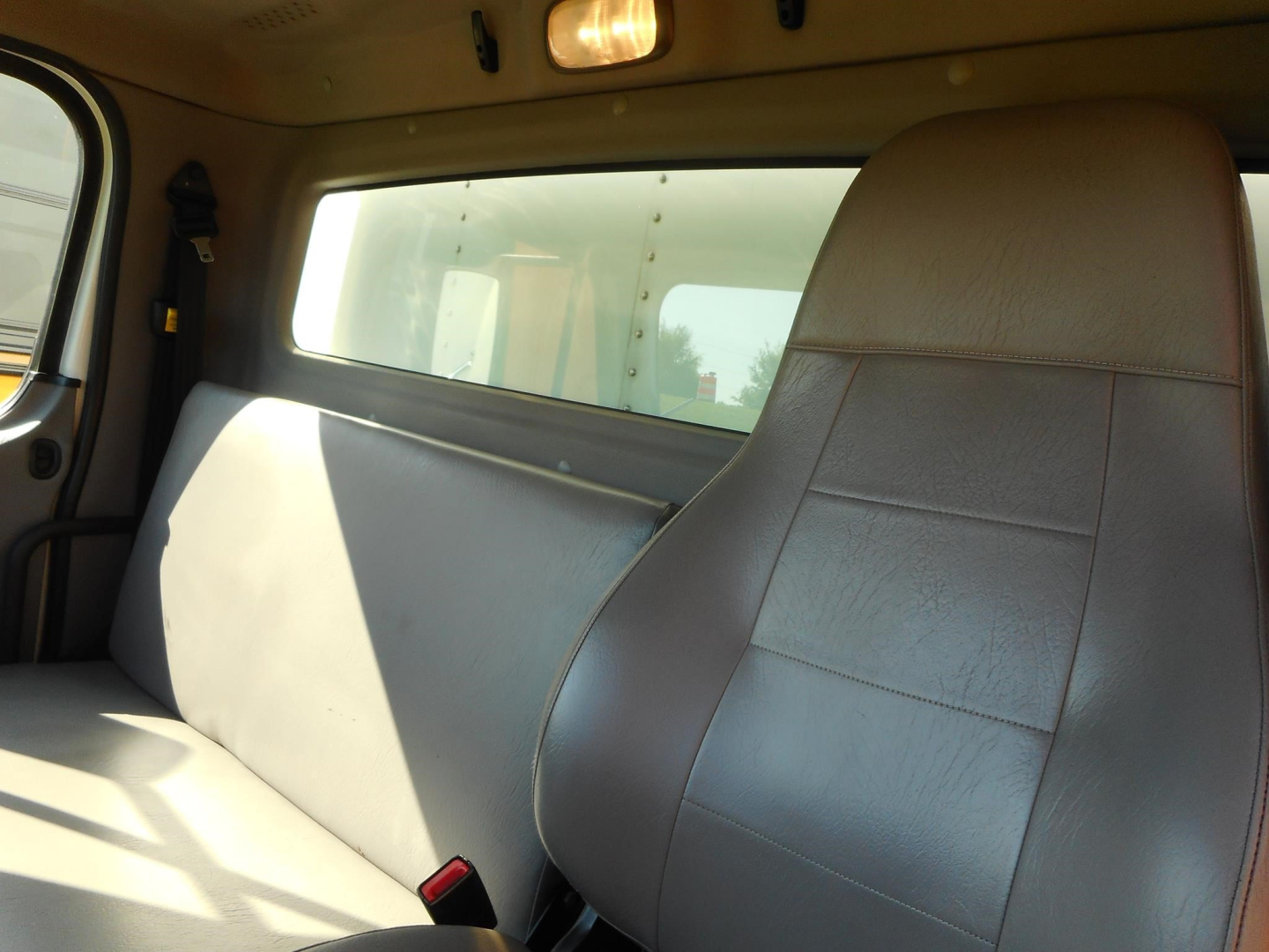 Truck cab interior showing grey seat with window and overhead light in Freightliner M2 106 cab interior.