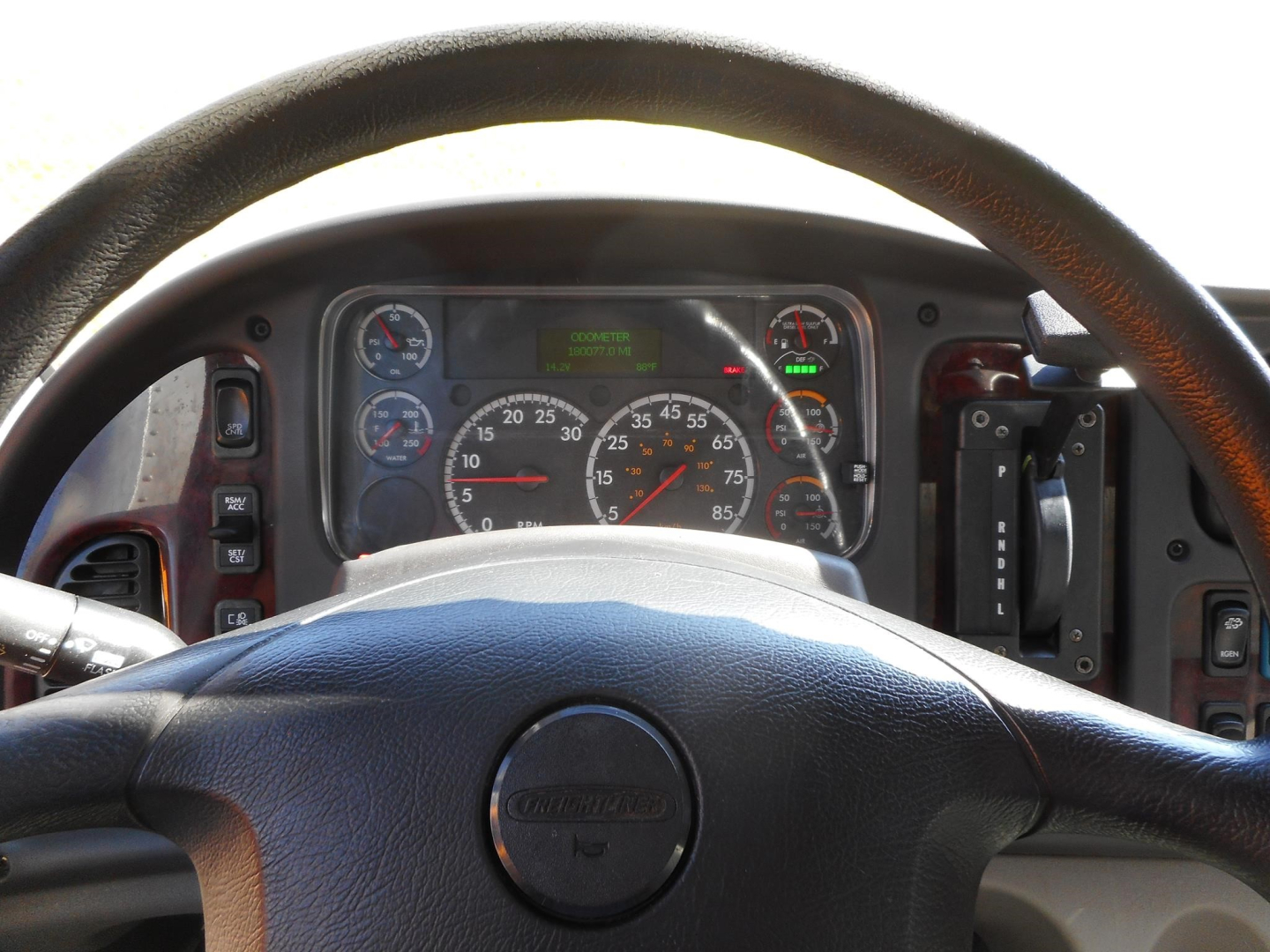 Dashboard view of a Freightliner M2 106 truck steering wheel and instrument cluster with gauges and digital display.