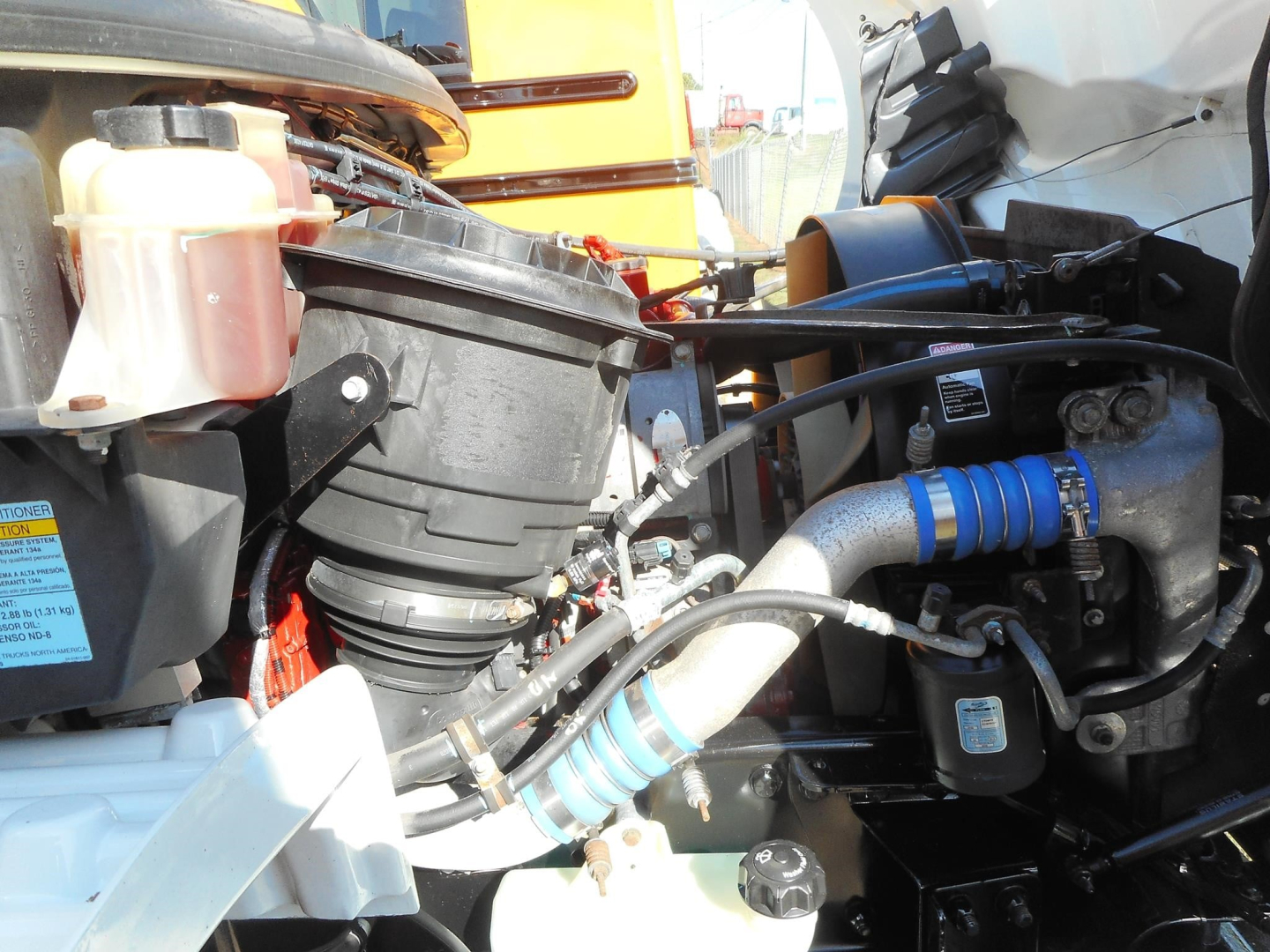 Engine bay of 2019 Freightliner M2 106 showing coolant reservoir, hoses, and turbocharger with blue silicone hose couplers.