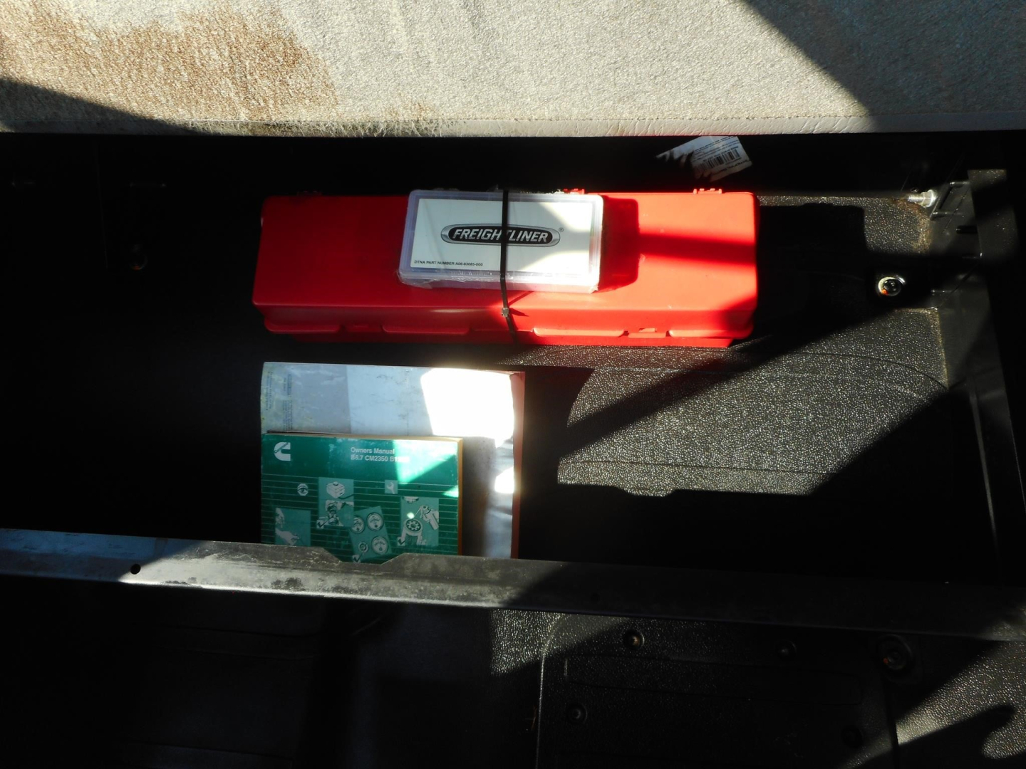 Trucks cargo area showing a red tool case labeled Freightliner and a green and white box in a storage drawer.
