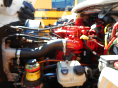 Engine bay of a 2019 Freightliner M2 106 truck showing red engine components, hoses, and fluid reservoirs with a white coolant reservoir and yellow oil filter cap visible.