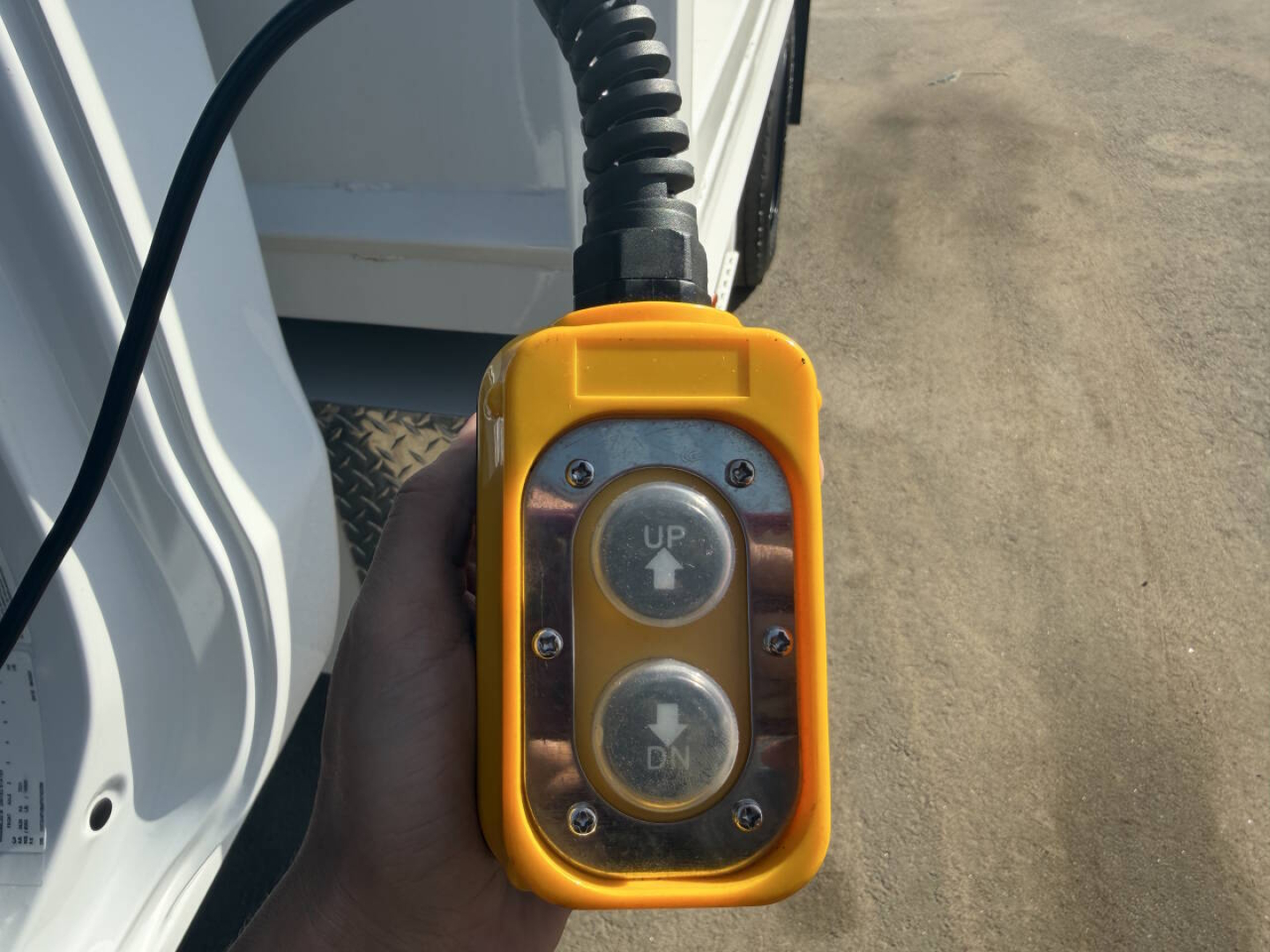 Truck exterior with a handheld control pendant showing UP and DN arrows, yellow rugged enclosure, attached to a cord near the cab.