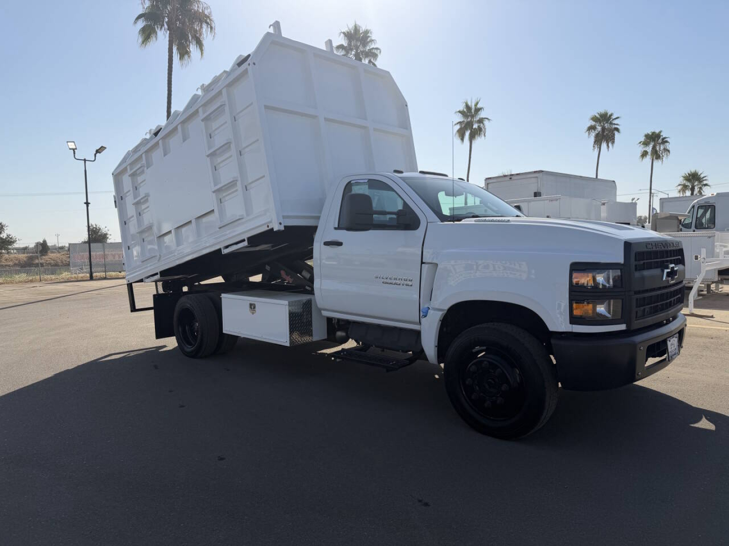 Chevrolet 6500 HD dump truck in a tilted dump bed with white cabin, black wheels, and clearance in a dealership lot.