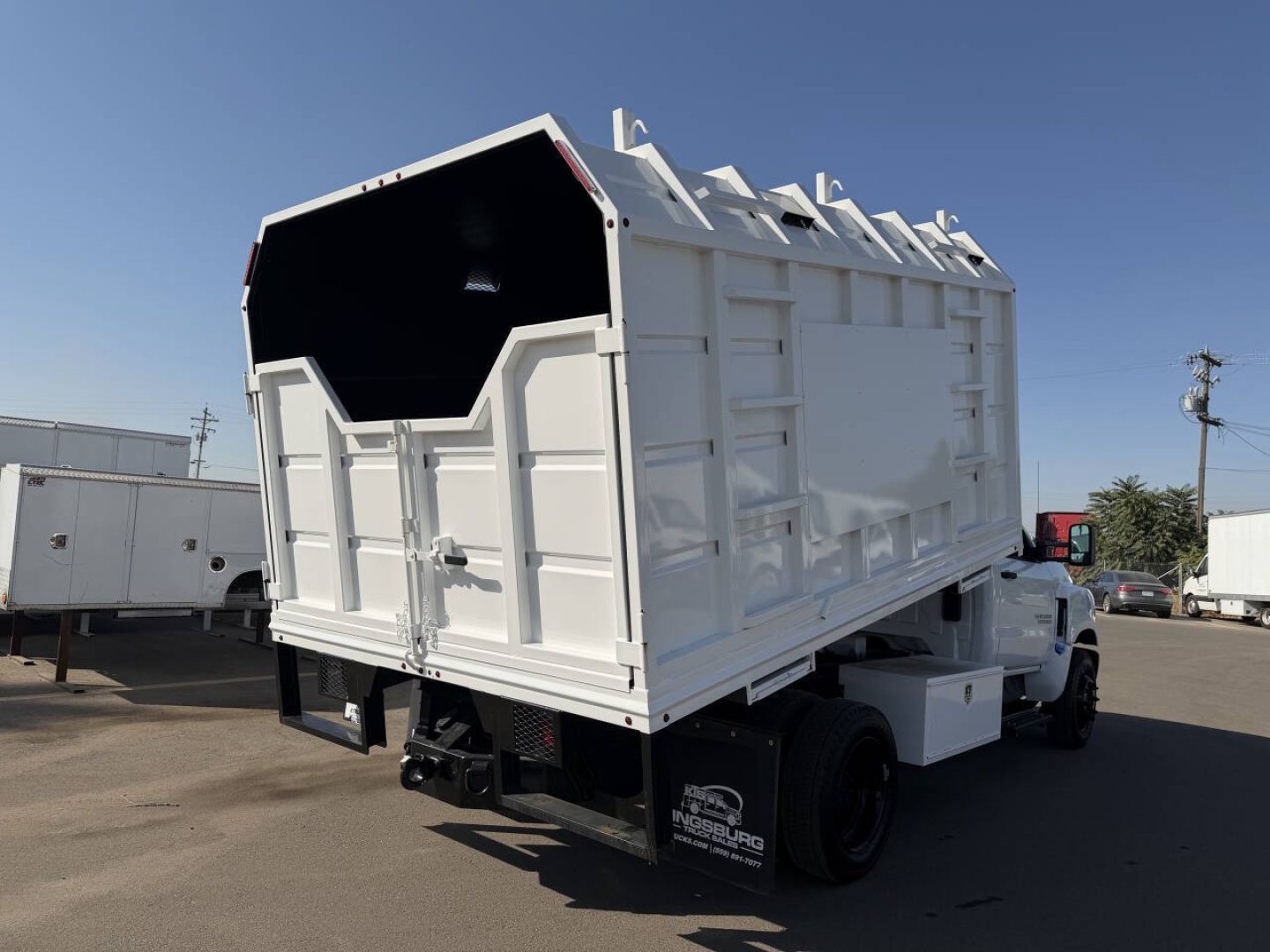 Truck rear and side view showing a white dumpster-style body mounted on a Chevrolet 6500 HD chassis with open top, chipper category vehicle.