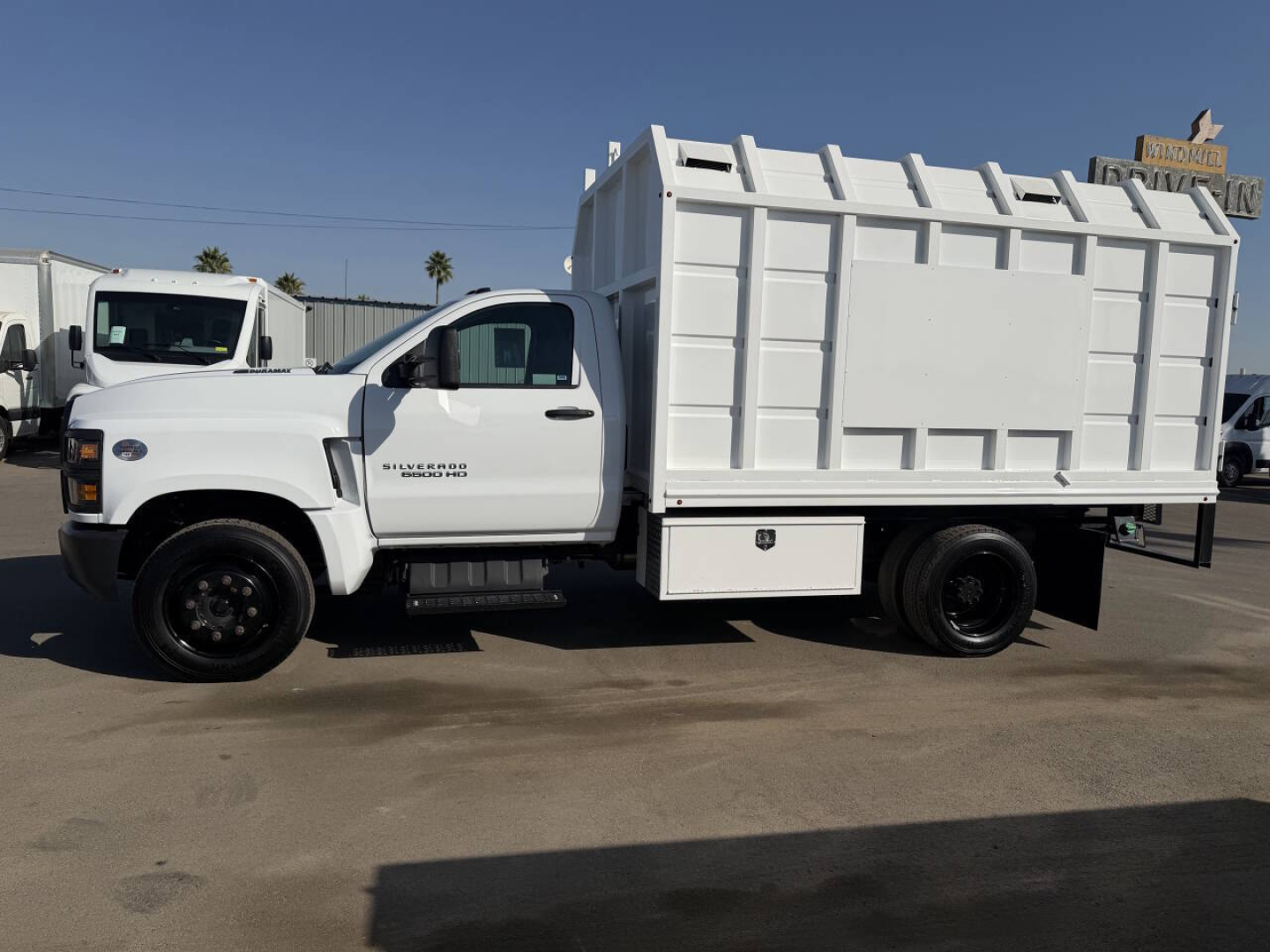 Truck side view showing a white 2023 Chevrolet 6500 HD with a large dump bed and utility compartments