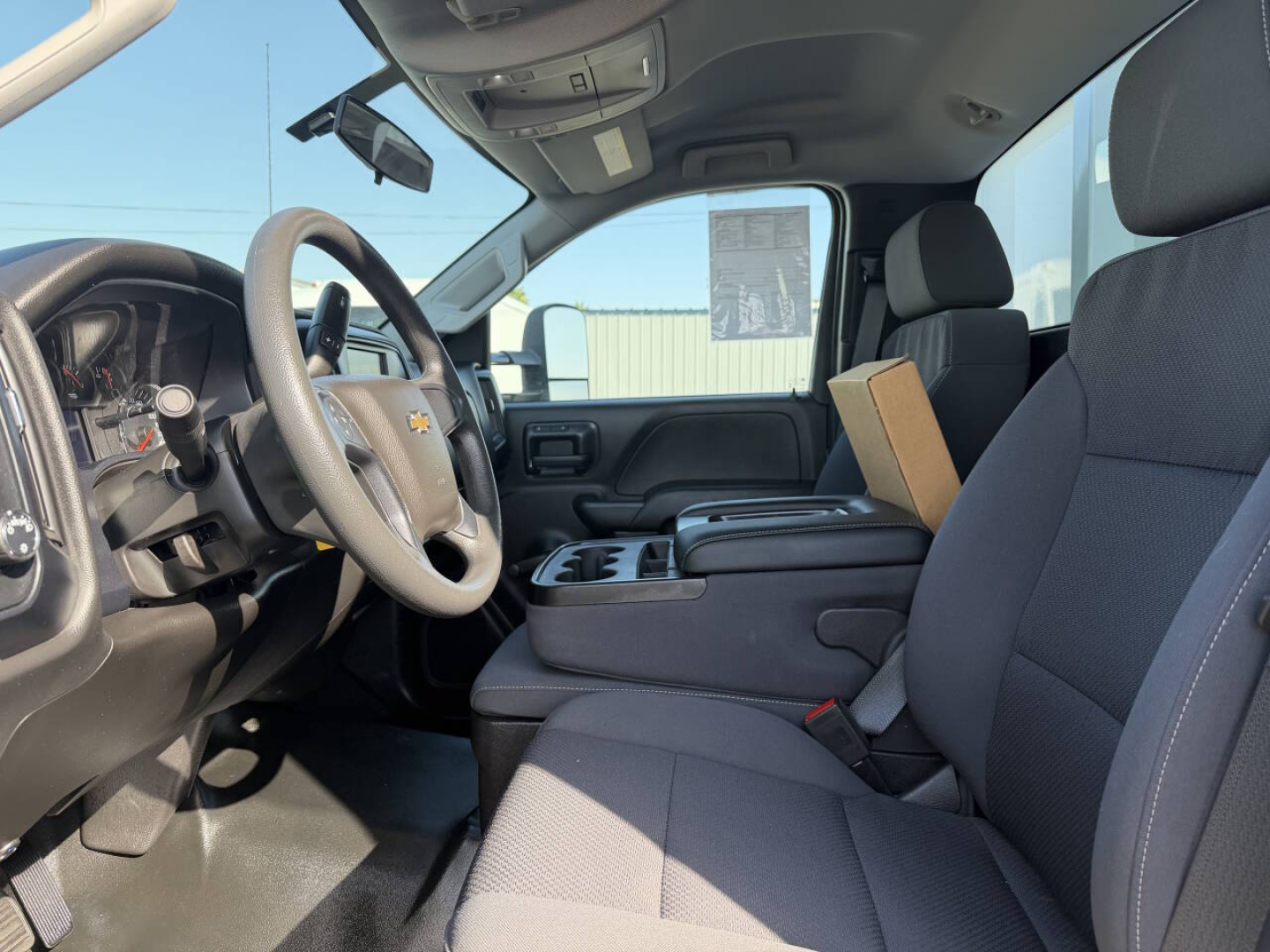 Interior cab view of a 2023 Chevrolet 6500 HD chassis-cab showing steering wheel, driver seat, center console, and dashboard with cup holders