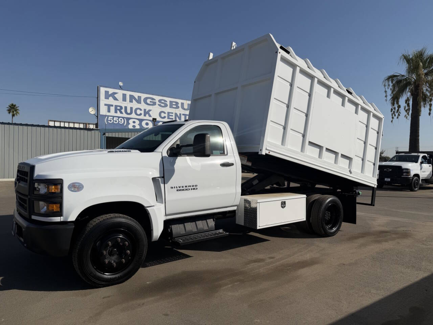 Truck with a raised dump bed in a dealership lot; visible text on side reads ‘New Mexico' not present; license text not clear. Primary legible elements are the truck itself and a sign in background partially reading ‘TRUCK CENTER’ and
