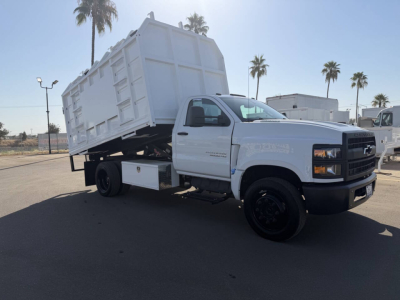 Chevrolet 6500 HD dump truck in a tilted dump bed with white cabin, black wheels, and clearance in a dealership lot.