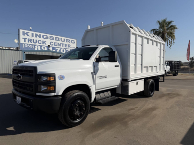 White 2023 Chevrolet 6500 HD dump truck in service with chipper body, side view showing cargo box and dual rear wheels.