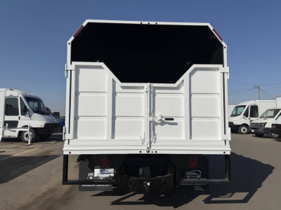 Rear view of a white 2023 Chevrolet 6500 HD truck with a dump bed, visible tailgate latch, bumper, and hitch, in a dealership lot.