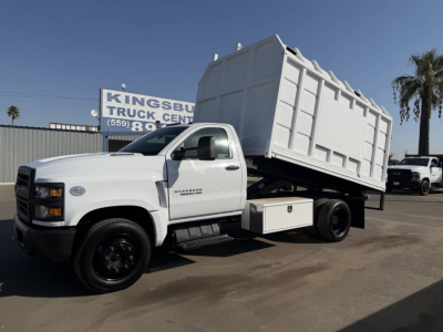 Truck with a raised dump bed in a dealership lot; visible text on side reads ‘New Mexico' not present; license text not clear. Primary legible elements are the truck itself and a sign in background partially reading ‘TRUCK CENTER’ and