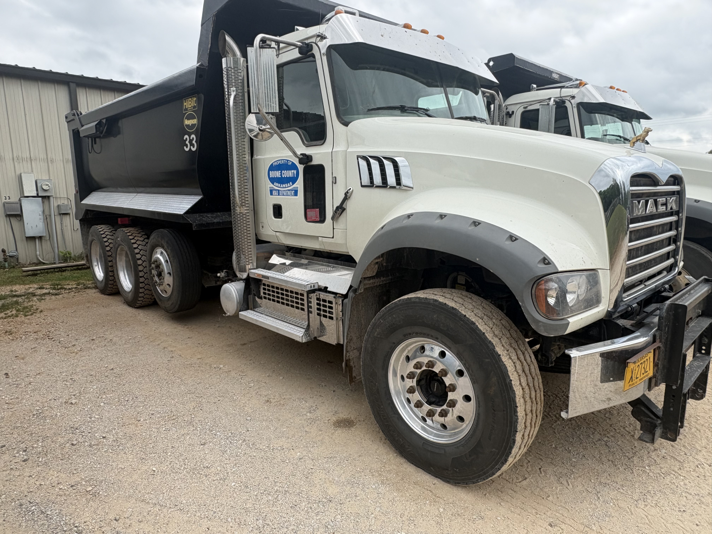Mack GR84F dump truck with white cab and black dump bed, side view showing front grille, dual exhaust, and steps.