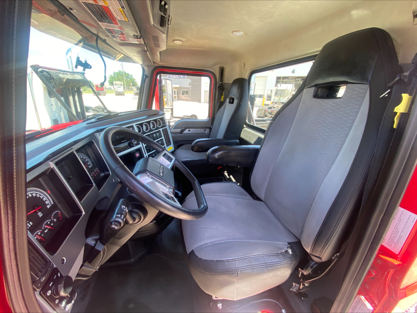 Truck cab interior view of a 2021 Mack AN64T showing steering wheel, dashboard, and front seats.