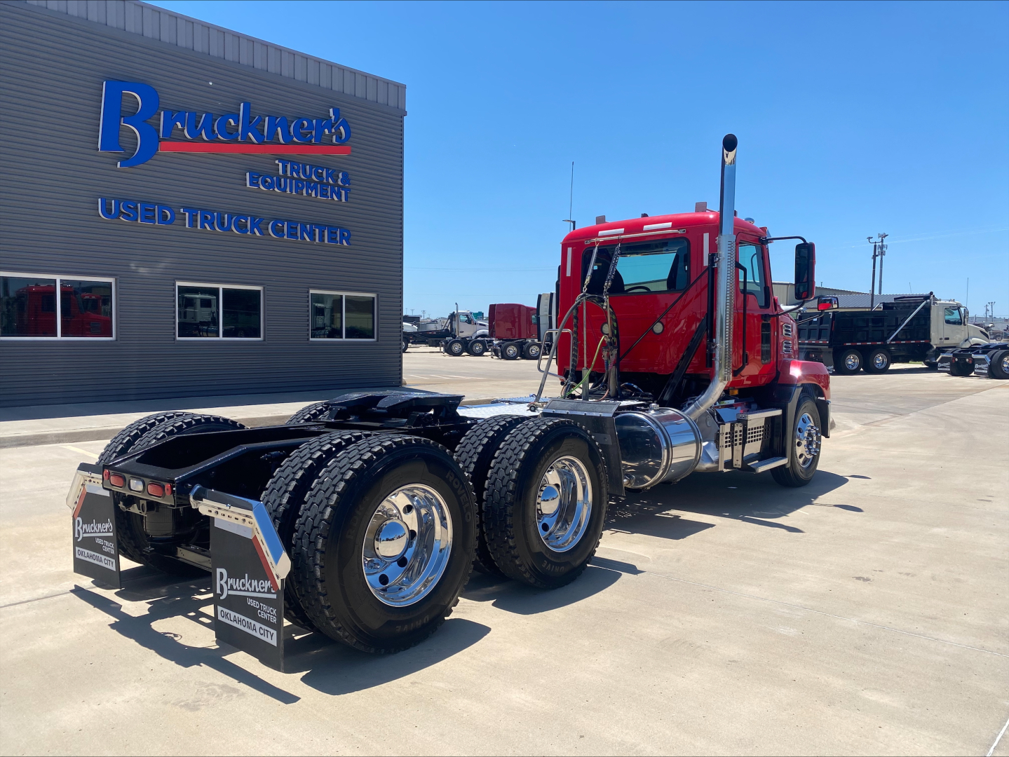 Truck tractor in red cab view from rear-left showing dual rear axles and fifth wheel; Mack AN64T branding not visible.