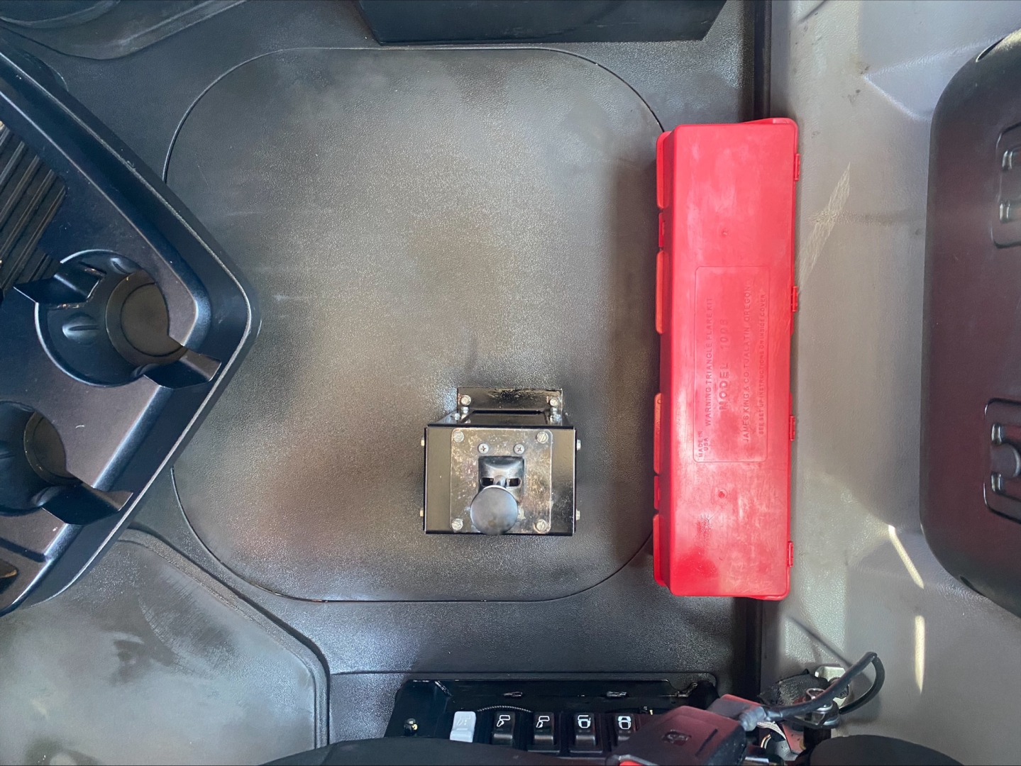 Conventional daycab interior view showing center floor area with a silver latch/lever, a red plastic toolbox, and control panel edges.