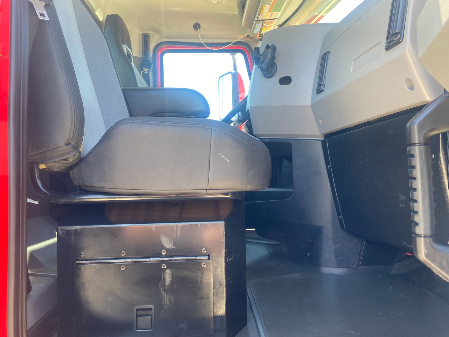 Cab interior of a Mack AN64T daycab showing driver's seat and dashboard with storage box under seat.