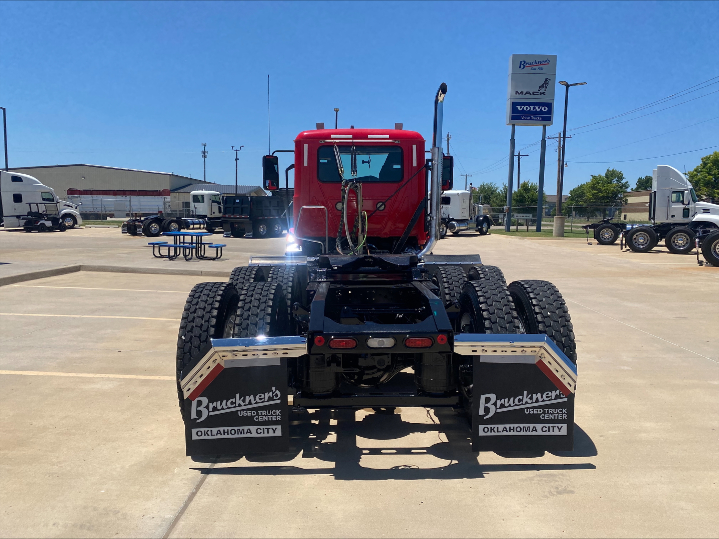 Rear view of a red 2021 Mack AN64T daycab tractor showing rear mud flaps with 'Bruckners USED TRUCKS OKLAHOMA CITY' text, and chassis details.