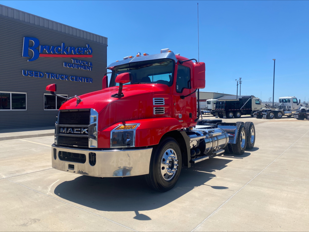Mack AN64T heavy-duty truck in red showroom at a used truck center, 6x4 conventional daycab drivetrain with chrome fuel tanks and dual rear axles.