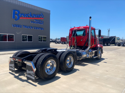 Truck tractor in red cab view from rear-left showing dual rear axles and fifth wheel; Mack AN64T branding not visible.