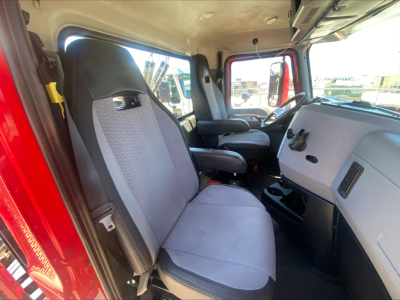 Truck cab interior showing the driver's seat and passenger seat with light gray upholstery, dashboard with steering wheel, door opening, and windows.