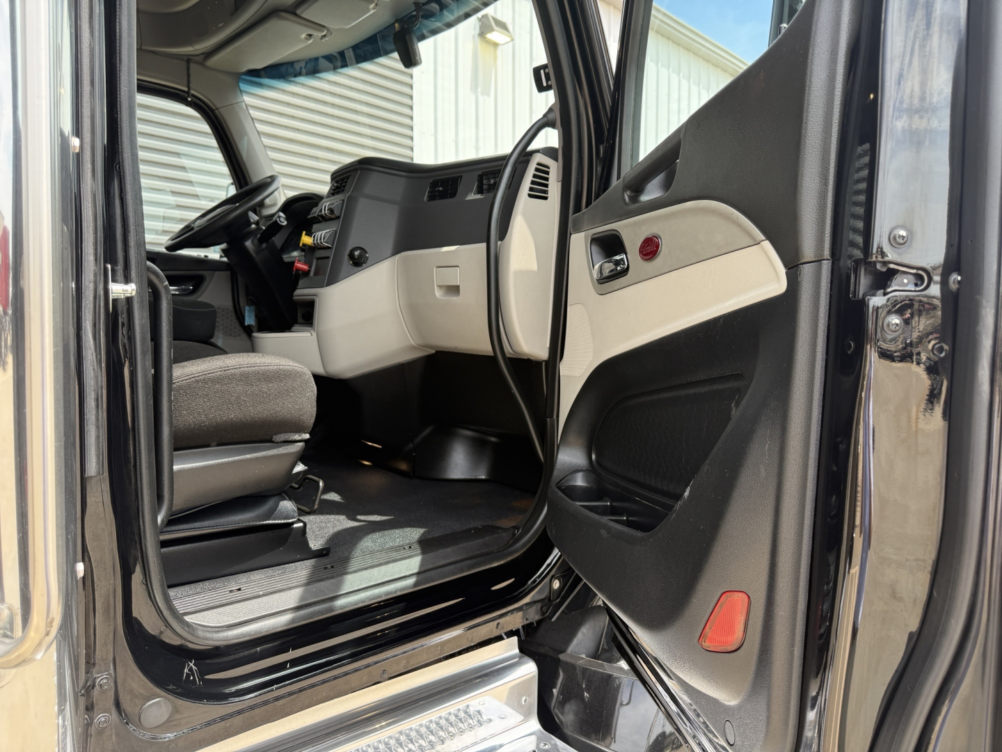 Peterbilt 579 cab interior with driver door open; dashboard, steering wheel, and beige interior trim visible.