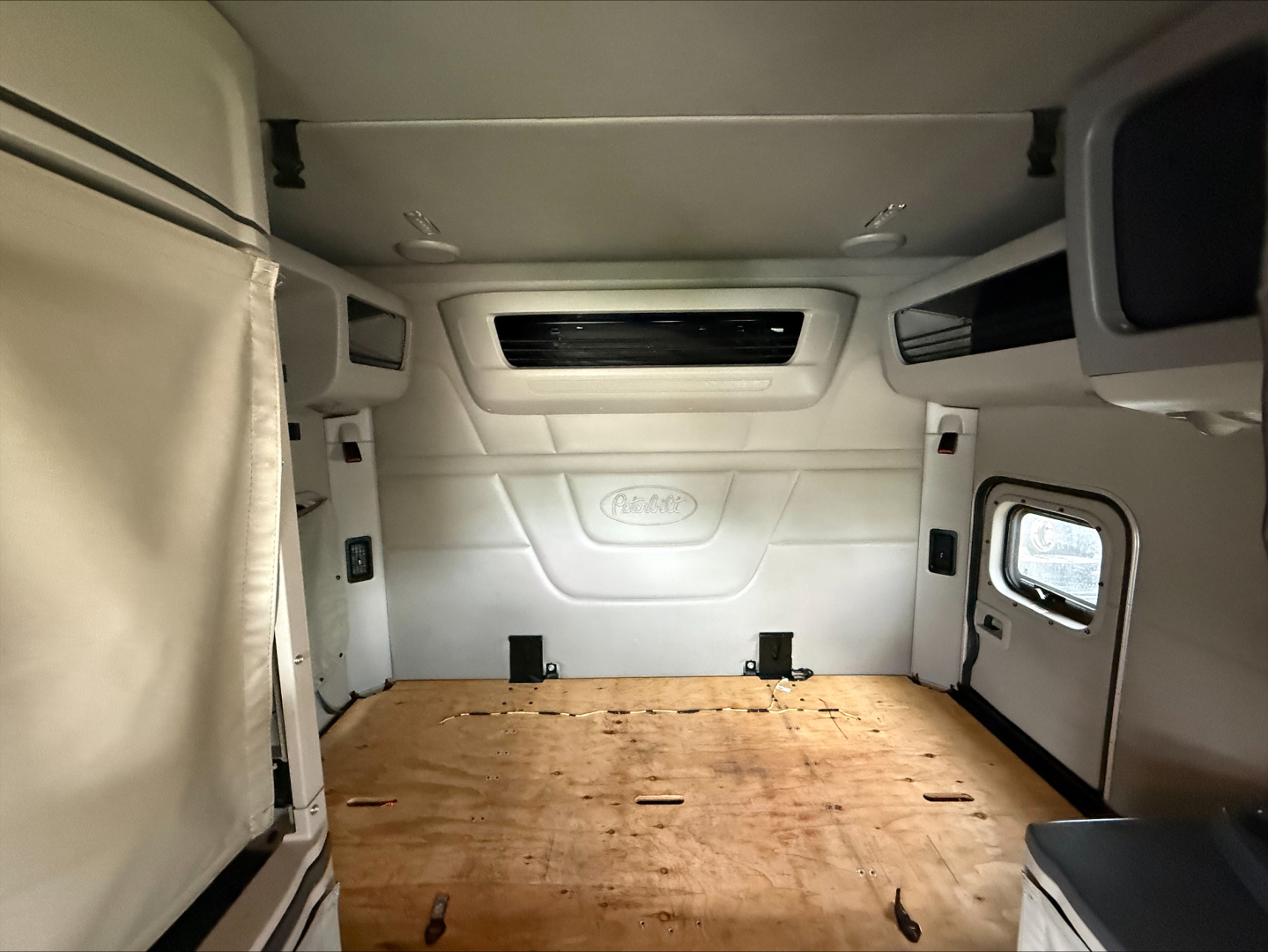 Peterbilt cab interior cargo area with wooden floor and white side panels, view from rear showing sleeper cab and side window.
