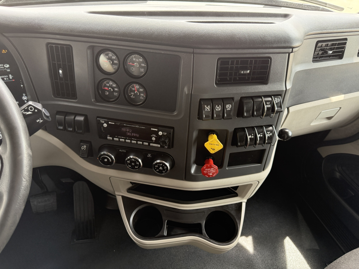 Peterbilt 579 dash area showing gauges and controls. Includes steering wheel left, multiple round gauges, switch panels, climate controls, and cup holders.