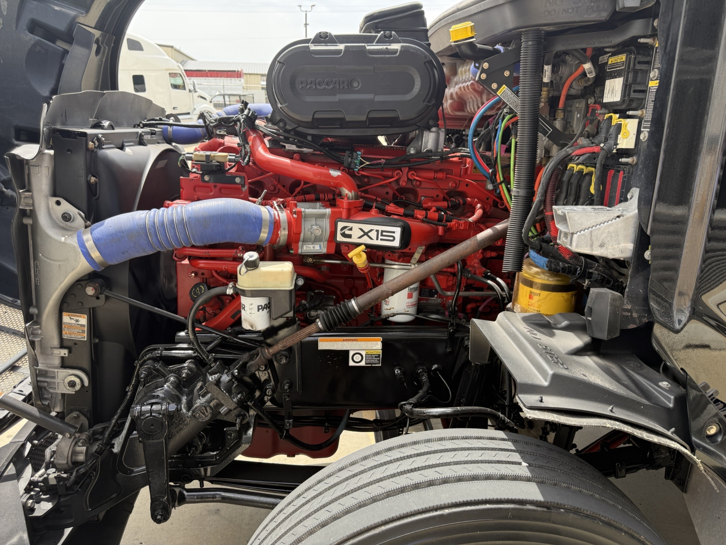 Peterbilt 579 engine bay with red engine block, blue hoses, and various wiring; visible label reads EX15 and other components around the cab interior.