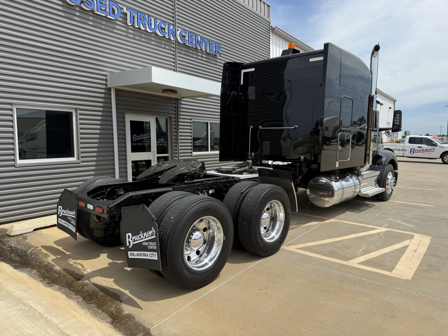 Peterbilt 579 tractor in-service showing dual rear axles, black sleeper cab, chrome fuel tanks, and fifth-wheel area at trucking lot.