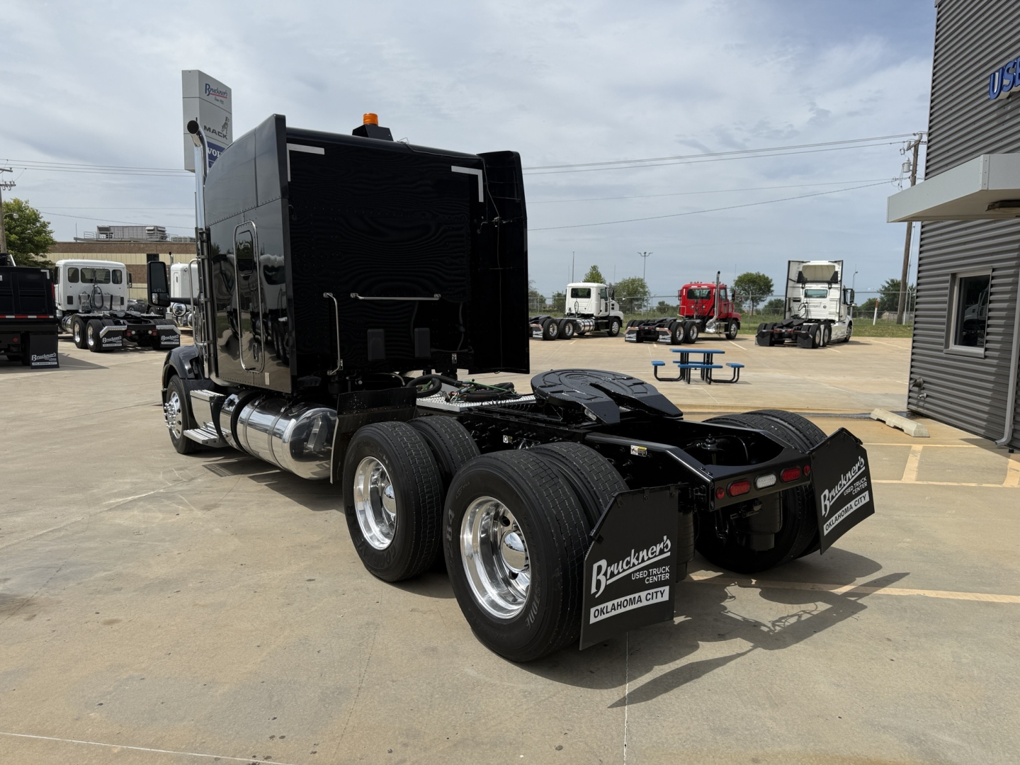 Peterbilt 579 tractor in a dealership lot, rear/side view showing dual rear axles and black glossy sleeper cab with chrome wheels.