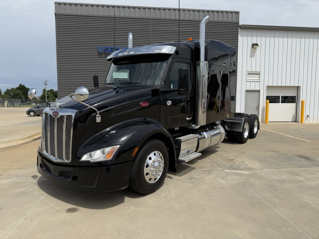 Peterbilt 579 semi-truck in black with sleeper cab, front angled view, chrome exhaust stacks, dual rear axles, daytime exterior