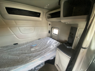 Peterbilt truck sleeper cab interior with bed and control panel; plastic-wrapped mattress visible.