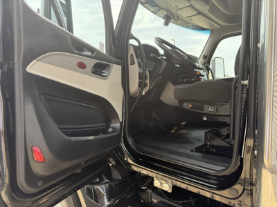 Truck cab interior of a 2022 Peterbilt 579 conventional sleeper showing driver seat, dashboard, and open door with interior panels.
