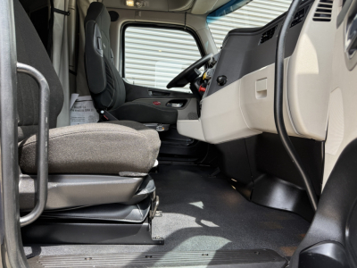 Peterbilt 579 truck interior driver seat and dashboard view from doorway, with steering wheel, gray and black cabin, front passenger seat, and floor mat visible.