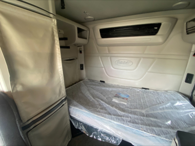 Peterbilt 579 sleeper cab interior showing cab wall with Peterbilt logo, window vent, and covered mattress in the sleeper area.