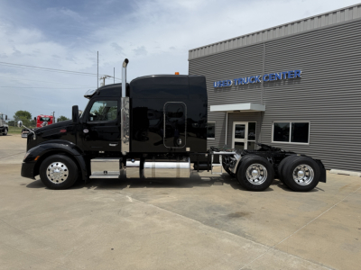 Peterbilt 579 truck tractor side view with sleeper cab and dual rear axles in front of Used Truck Center building.