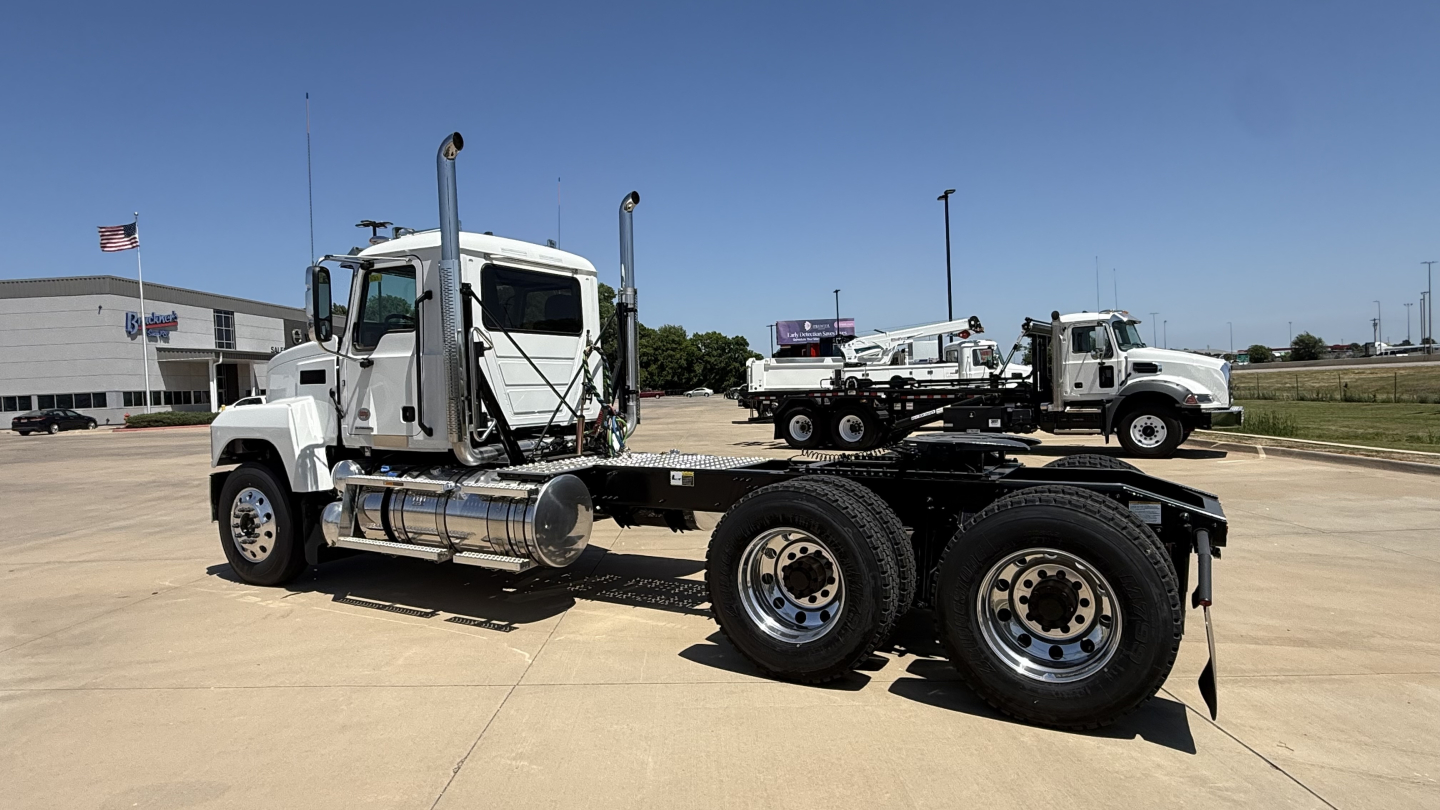 Semi truck tractor with a lowboy trailer, front cab and dual rear axles, chrome fuel tanks, exhaust stacks, and a Mack PI64T on a tilt bed trailer.