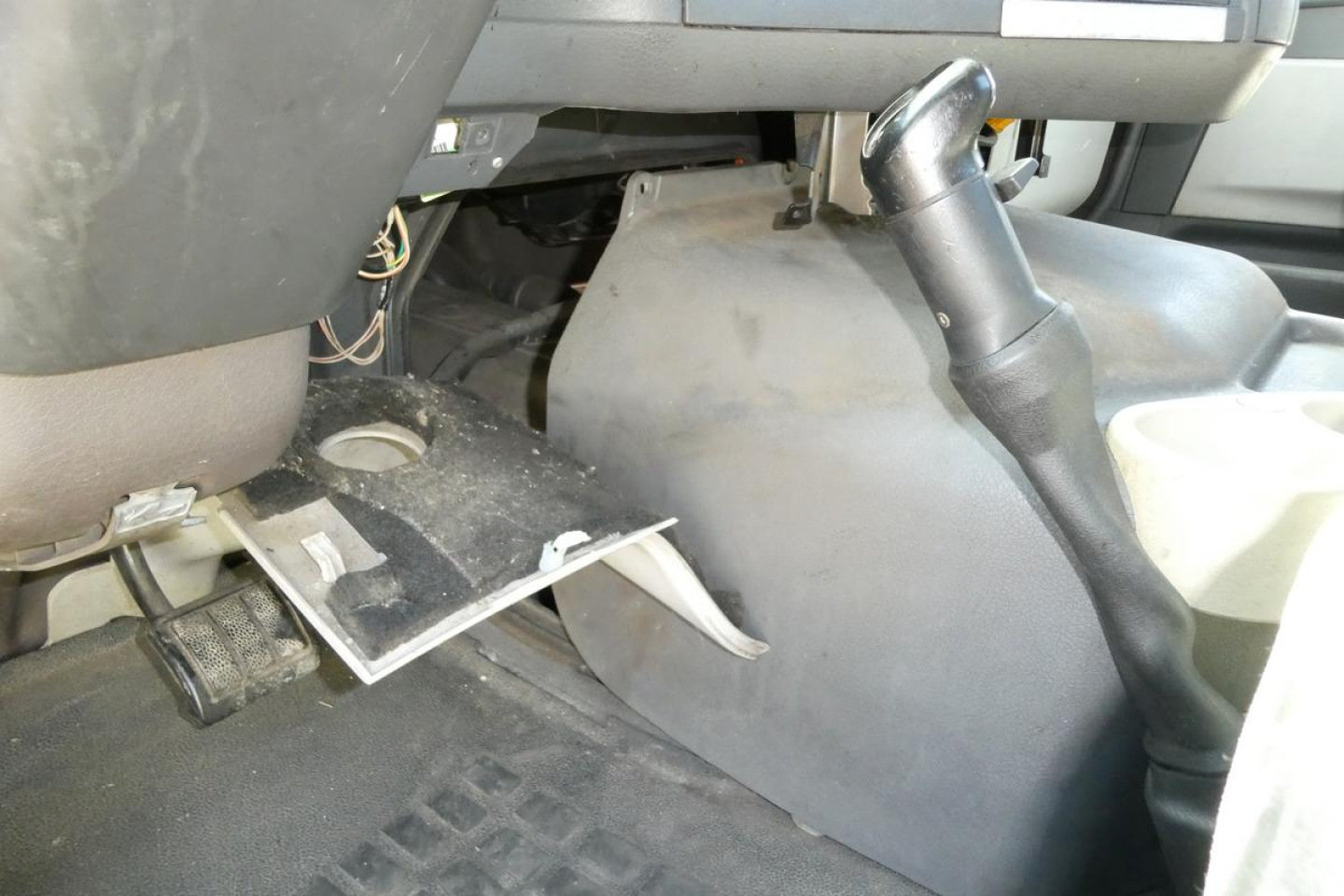 Volvo truck cabin interior showing steering column, floor pedals, and dashboard area with exposed wiring and a detached panel.