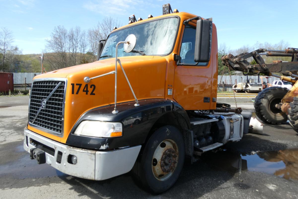 Volvo VNM42T conventional daycab truck showing orange cab with black fenders and wheel wells, number 1742 on door, front grille, side mirrors, and heavy-duty chassis.