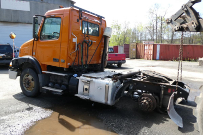 Orange Volvo VNM42T daycab truck with exposed drivetrain and cab side, VIN plate and stock tag visible.