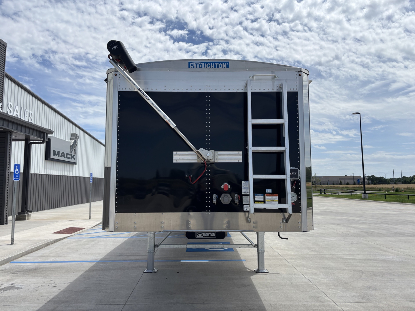 Stoughton aluminum grain hopper trailer rear view showing a 74" side height, ladder on right, rear door with crossbars, and a tilt chute with a support arm.