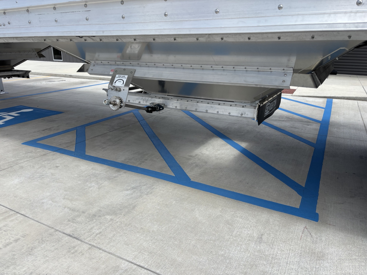 Trailer underside showing bulk grain hopper connection with a measurement gauge and metal frame, isolated in a parking area.